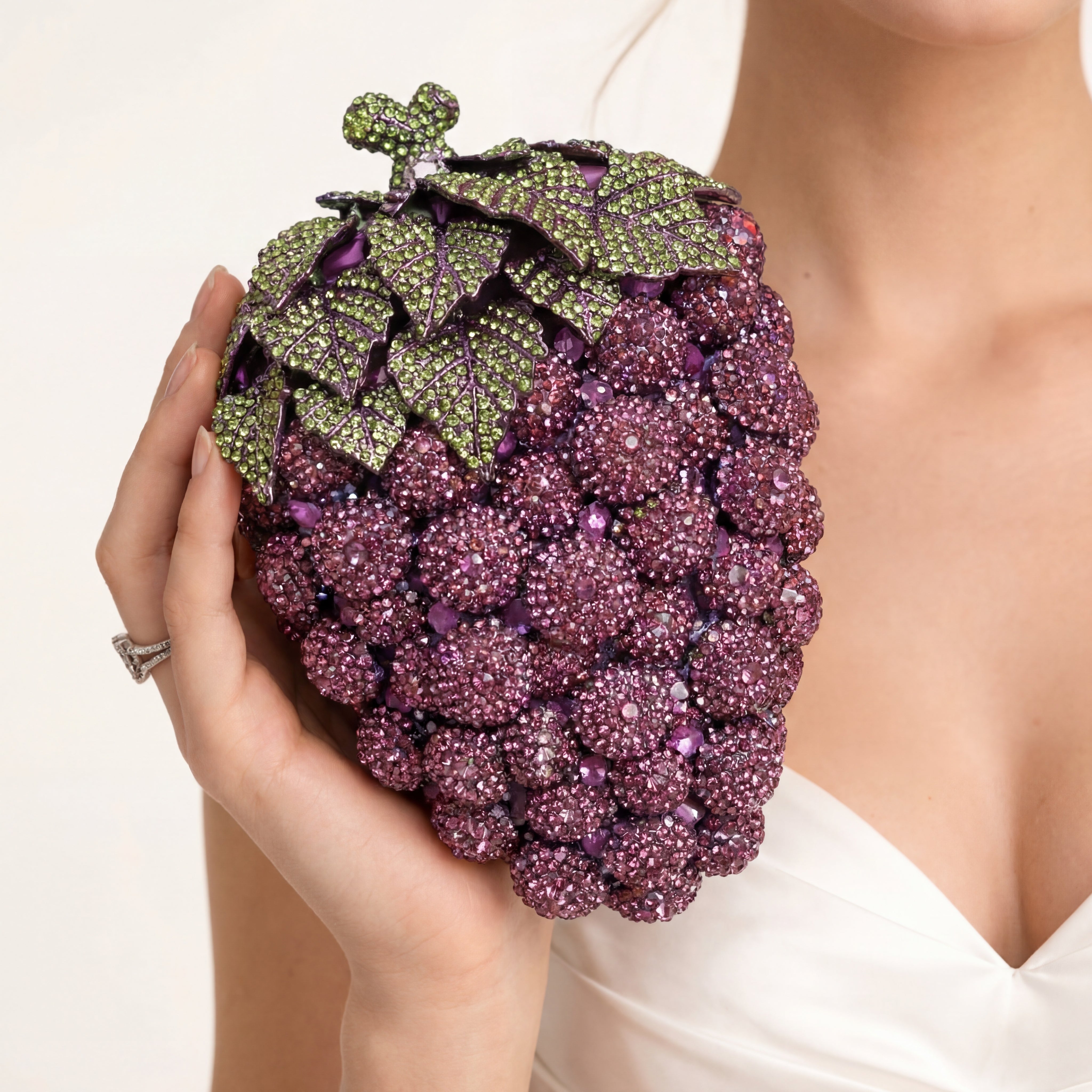 Purple grape-shaped clutch held by a hand against a white background